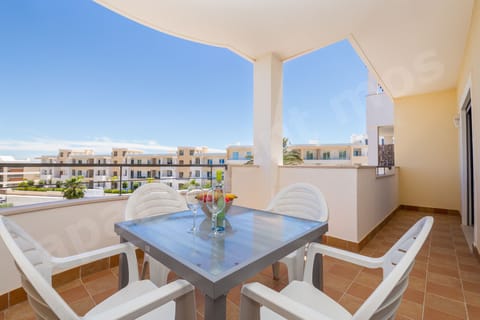 Covered balcony with outdoor dining table and chairs at Apartment Mos, a professionally cleaned 2-bedroom holiday apartment in the Algarve, Portugal, featuring views of the communal pool area and surrounding gardens