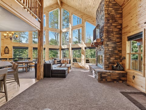 Sink into the sofa and let sunlight flood this soaring living room, where a stunning stone fireplace anchors your mountain retreat and forest views frame every moment of relaxation.