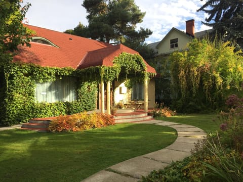 Curved concrete path leads to a red-shingled porch draped with green ivy and framed by lush garden beds.