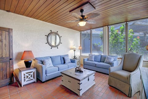 Your spacious living area features coastal charm with blue sofas, nautical accents, and garden views through large windows.
