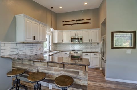A modern kitchen with white cabinets, a subway tile backsplash, and granite countertops. The island features a rustic wooden front with three round wooden stools. Stainless steel appliances are present.
