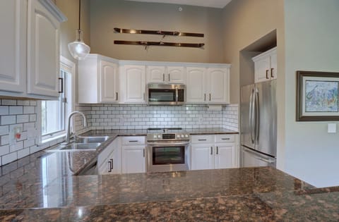 Modern kitchen with white cabinets, stainless steel appliances, mosaic tile backsplash, and dark granite countertops. A pair of vintage skis decorates the wall above the cabinetry.