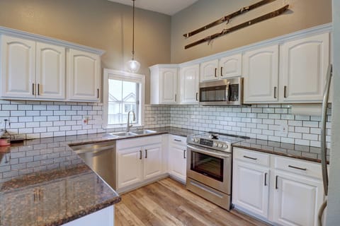 A modern kitchen with white cabinets, stainless steel appliances, granite countertops, and a subway tile backsplash. Two vintage skis are mounted on the wall above the cabinets.