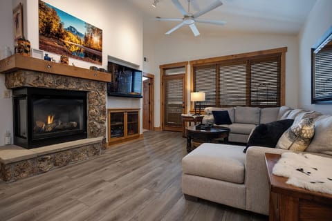 Cozy up by your crackling fireplace as mountain light filters through wooden blinds in this inviting living space.