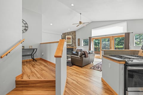 Welcoming entryway with warm hardwood floors leading to a spacious living area. Features a cozy stone fireplace, vaulted ceilings with a ceiling fan, and expansive windows that open to a private deck with serene forest views. Perfect for relaxing after a d