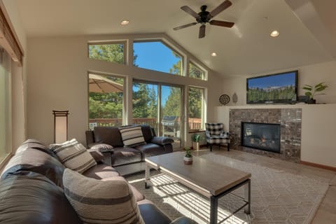 - Living room with vaulted ceilings and fireplace warmth  
- Large windows with forest views and natural light  
- Cozy leather sofas and flat screen TV setup