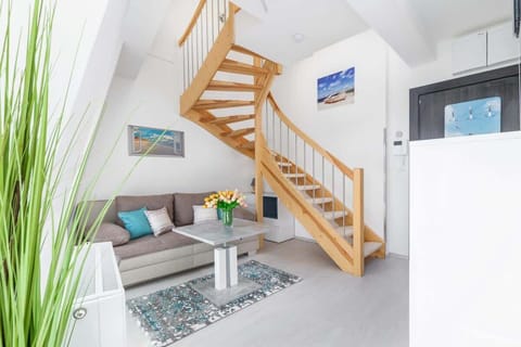 A cozy living room with a staircase leading to an upper floor. The room is decorated with plants and has a bright atmosphere.