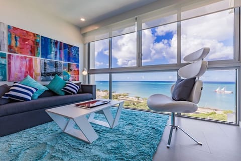 Picture yourself lounging on a plush sofa surrounded by vibrant art while gazing at stunning turquoise waters stretching endlessly before you—your perfect coastal escape awaits.