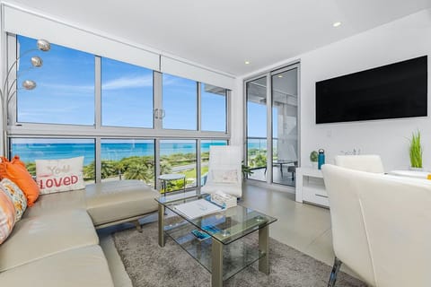 Your modern living space opens to breathtaking ocean views through floor-to-ceiling windows, where bright blue waters meet the horizon and soft coastal breezes await just beyond your private terrace.
