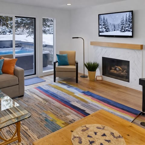 Unwind in the cozy, modern living area featuring a warm fireplace and large glass doors leading directly to your private outdoor hot tub with scenic views.