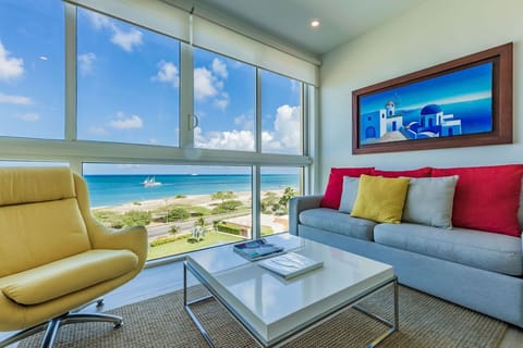 Picture yourself here: bright, breezy living room where vivid pops of color meet sweeping ocean views through floor-to-ceiling windows—your perfect retreat for sun-soaked relaxation.