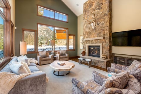 Sink into plush seating by your crackling stone fireplace while soaring windows frame stunning mountain views in this cozy yet elegant living space.