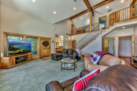 Living room with vaulted ceilings, wood beams, leather and fabric sofas, and a large flat-screen TV on a wooden cabinet.
