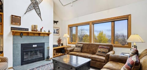 Spacious main living area with vaulted ceilings, fireplace, comfortable seating, and beautiful mountain views through oversized windows.