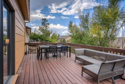 Spacious wooden deck with outdoor dining table and cushioned seating, a welcoming spot to sip morning coffee or gather for an open-air meal while enjoying the surrounding trees and blue sky.