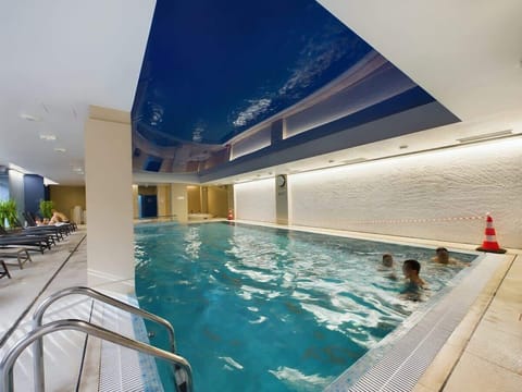An indoor swimming pool with blue tiles and a relaxing atmosphere, featuring lounge chairs in the background.