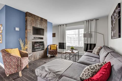 Cozy living room with sectional sofa, electric fireplace, flat-screen TV, and natural light.