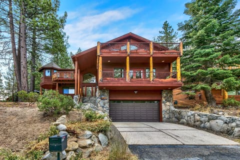 Exterior view of a multi-level wood house with stone accents, a double garage, and decorative wooden balcony railings.