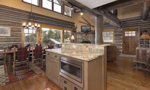 Gather in this stunning rustic kitchen featuring stone fireplace, granite island, and authentic log cabin charm perfect for memorable meals.