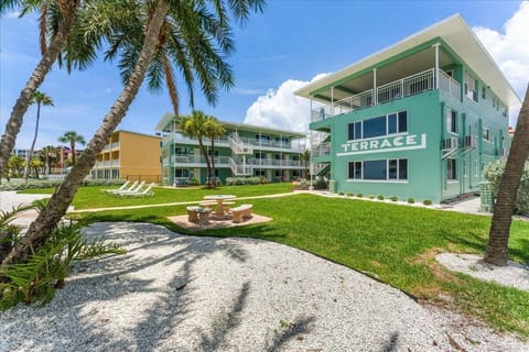 A beautifully landscaped tropical courtyard with stone patio seating, swaying palms, and stunning Gulf views