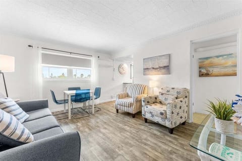 Bright, open living room with smart TV, sofa bed, coastal décor, and a dining area — a comfortable space to relax or gather after a day at the beach.