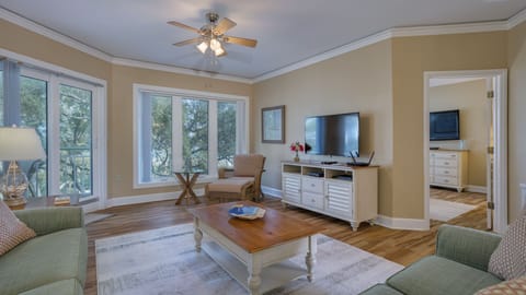 This spacious living area features plush seating, a large smart TV above a decorative fireplace, and a seamless flow into the dining and kitchen spaces