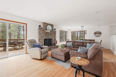 - Open living space with sectional and recliner  
- Stone fireplace adds rustic cabin charm  
- Sliding doors lead to deck with forest views