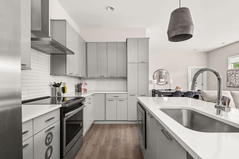 Stylish modern kitchen with sleek gray cabinetry, quartz countertops, stainless steel appliances, and an open layout to the dining and living areas.