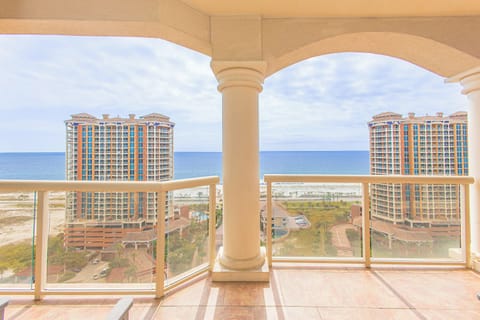 A covered balcony overlooking the Gulf Coast, framed by elegant arches and columns, showcases sweeping views of the ocean, neighboring resort towers, and beachfront grounds.