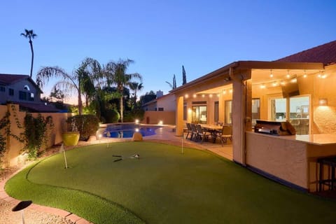 Private backyard paradise featuring a pool, sun loungers, mini golf, a covered patio with an outdoor dining area, and a BBQ with bar seating.