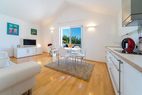Kitchen with dining table and chairs next to the living room with sofa and TV and access to the fenced terrace of the luxury villa Primosten Oasis