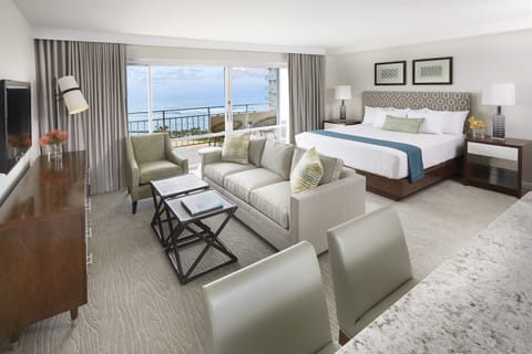 Step into your spacious suite where plush seating invites you to unwind, a king bed promises restful nights, and your private balcony frames endless ocean vistas just beyond the glass.