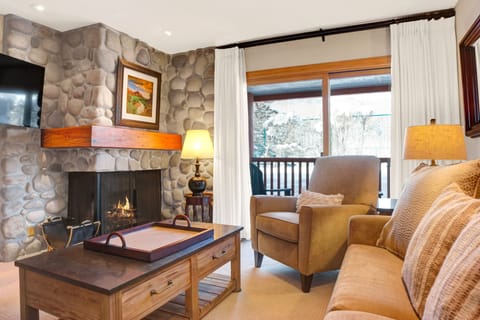 Living room features a gas fireplace with beautiful river rock surround and access to the private patio through the sliding glass doors