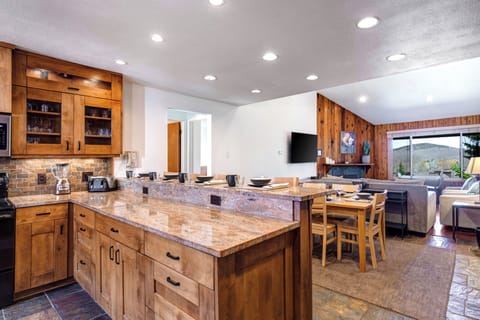 The kitchen breakfast bar has warm toned granite counters and wood cabinets, and has place settings for 4 guests.