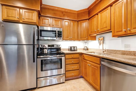 Medium toned wood cabinets with stainless steel appliances, under cabinet lighting and white walls.