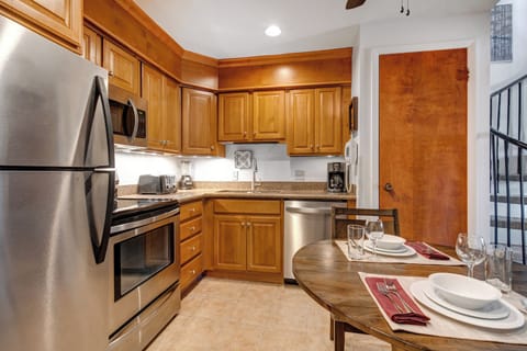 Medium toned wood cabinets with stainless steel appliances, under cabinet lighting and white walls.