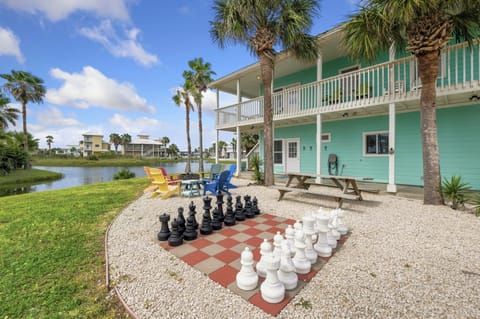 This charming beach house sits along a tranquil lake, offering colorful Adirondack chairs, outdoor chess, and picnic tables under swaying palms for relaxed fun in the sun.