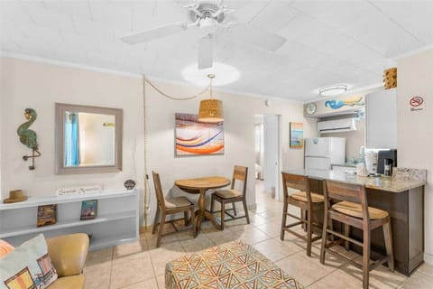 Open living and dining area with round table, granite breakfast bar with seating, AC unit, and cheerful coastal touches throughout.