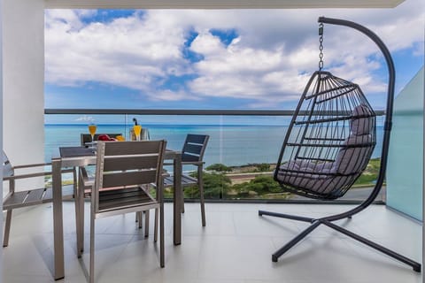 This private balcony offers breathtaking ocean views framed by azure skies, with a stylish dining setup and a cozy hanging chair perfect for relaxation.