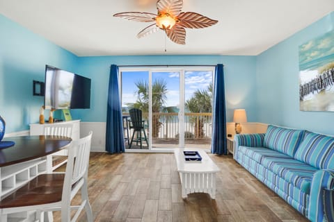 Relax in your bright coastal living room with stunning balcony views of swaying palms and blue skies.
