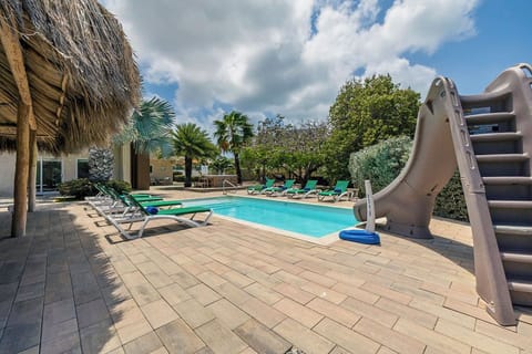 A serene poolside setting with plush sun loungers lined up under the radiant Aruba sun, inviting guests to soak in the tropical warmth. The crystal-clear pool water shimmers, reflecting the endless blue sky