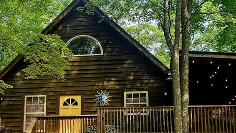Dark wood-paneled cabin exterior with pale yellow door, sun-and-moon wall decor, and railing-surrounded porch.