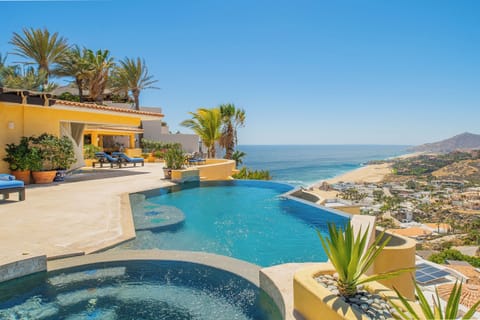 Stunning infinity pool overlooking azure waters and golden coastline, surrounded by tropical palms and luxurious outdoor lounging spaces.