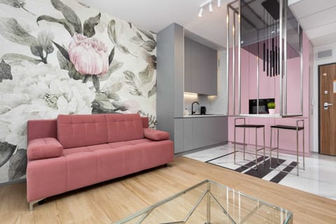A cozy living room featuring a pink sofa, floral wallpaper, and modern furniture, including a glass coffee table.