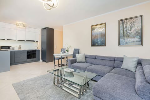 A bright and comfortable living room featuring a stylish gray sofa, a glass coffee table, and elegant wall art.