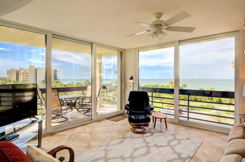 Living room with tan tile floors, black leather recliner, glass TV stand, and sliding doors opening to balcony views.
