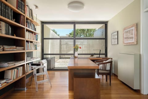 An office with an oak wood desk, a library, and a stylish recliner opens to the private patio
