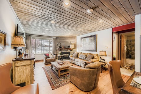 Relax in your cozy living room featuring rustic wood beam ceilings, a stone fireplace, and comfortable leather seating perfect for unwinding after mountain adventures.