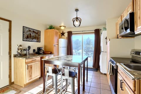 - Sunny eat in kitchen features a granite top island with stools and rustic wood cabinetry
- Full size fridge, coffee maker, and antler style lighting bring cabin warmth
- Sliding glass doors open to views and easy access to the outdoor patio