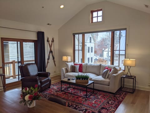 The living room is open and bright. Blinds on each window for privacy.